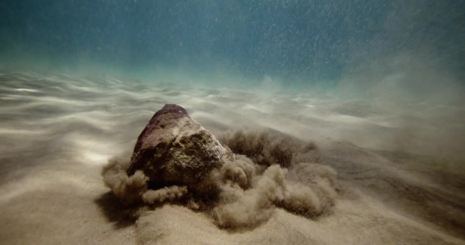 Rock falling into the depths of the ocean and hitting the sand