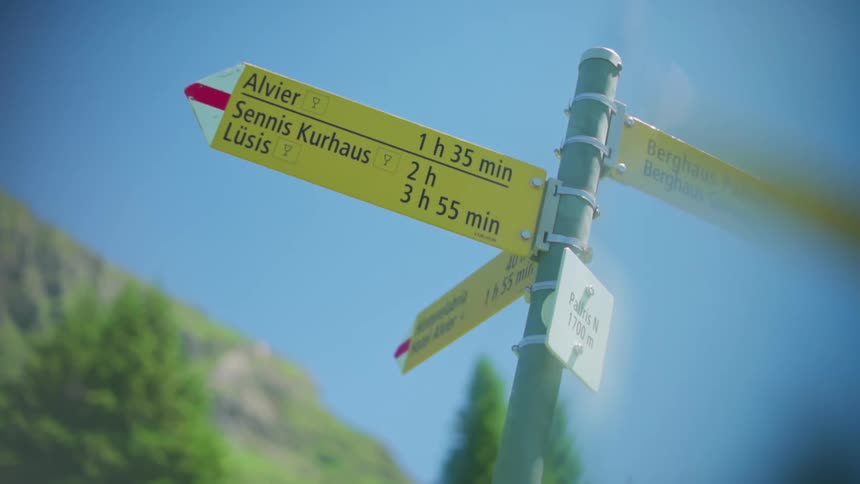 Yellow sign indicating trails and walking times in a mountainous region