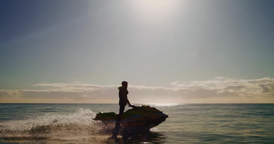 Person wearing a life jacket standing on a jet ski moving through the ocean