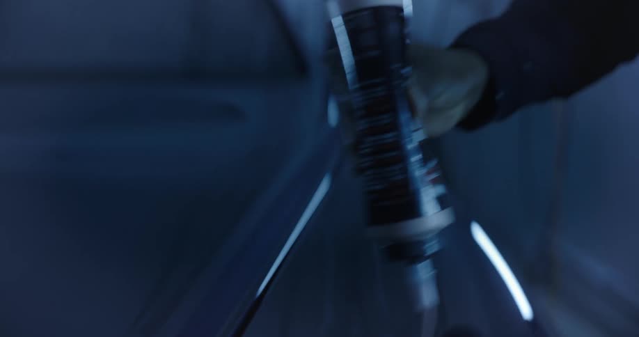 Hand taking a tube and applying white silicone to the hood of a vehicle