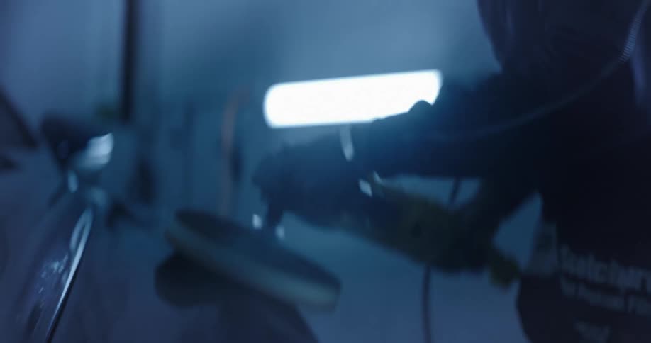 A man is using a power tool to polish the surface of a car in a garage or workshop setting