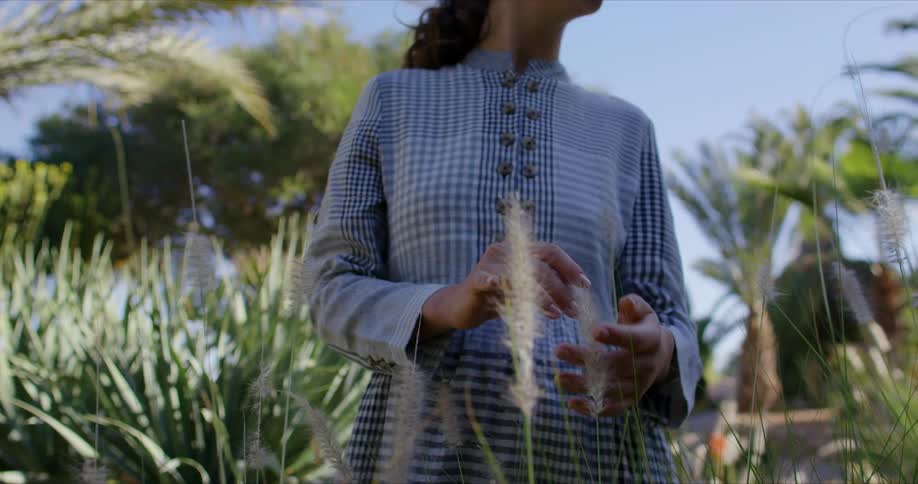 Woman in plaid dress running her hand through reeds outdoors