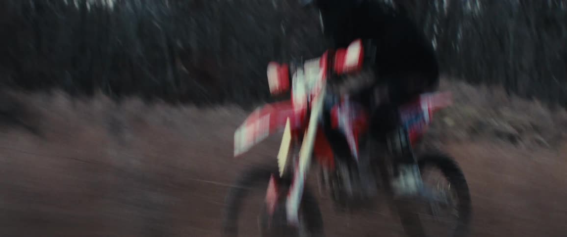 A man is doing jumps by the forest on his dirt bike