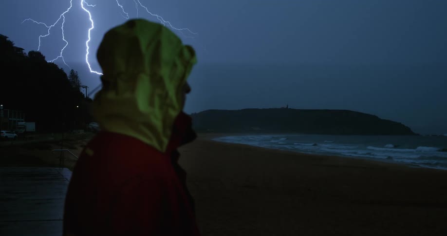 Man in jacket watching the sea from the sand on a thunderous night