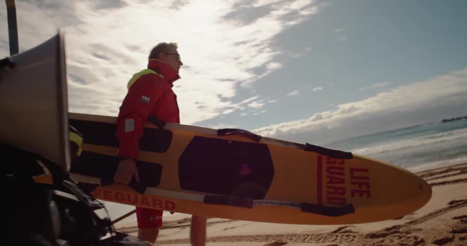 Lifeguard carrying a kayak walking across sand near the shoreline