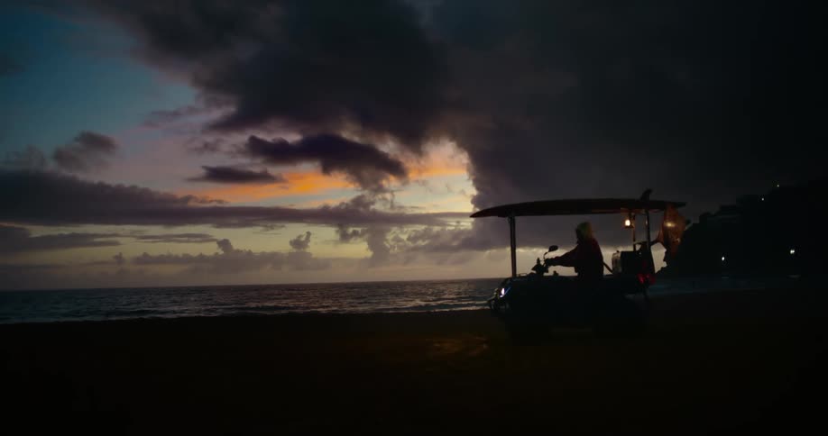 Silhouette of a patrol vehicle on the beach at dusk with a colorful sky and heavy clouds