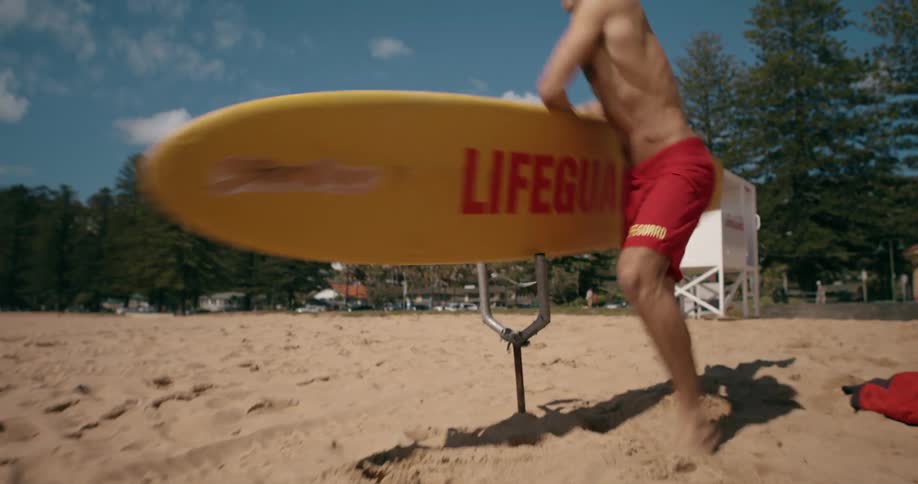 Lifeguard running to pick up a surfboard on the beach sand