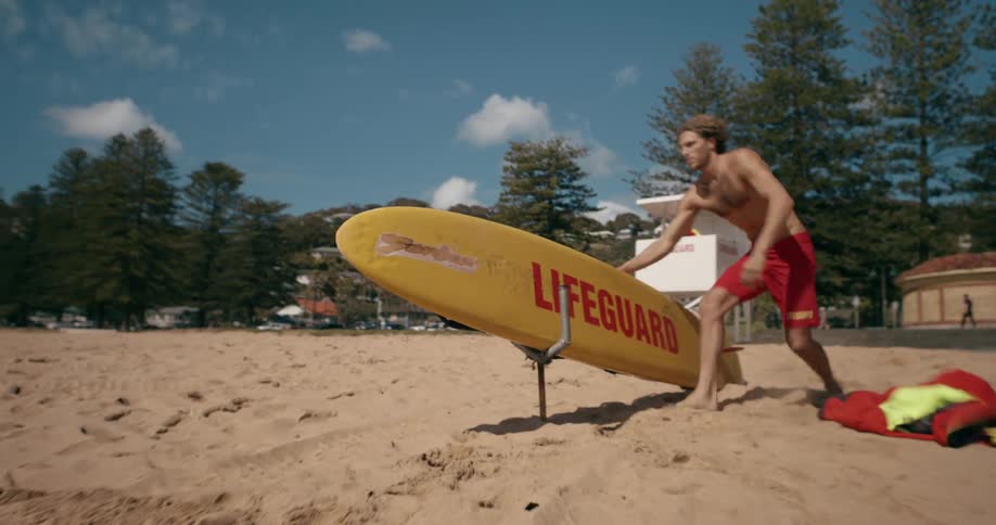 A lifeguard throws a jacket in the sand and picks up a yellow surfboard while running