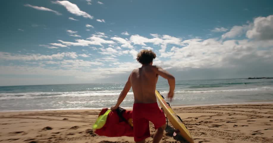 Man running on the sand taking off his jacket and grabbing a lifeguard board