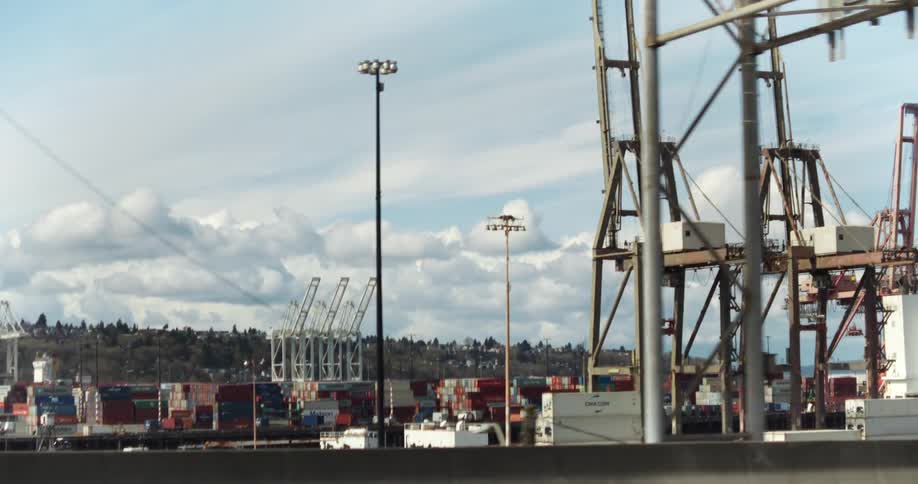 Cranes and containers at a busy port under a partly cloudy sky
