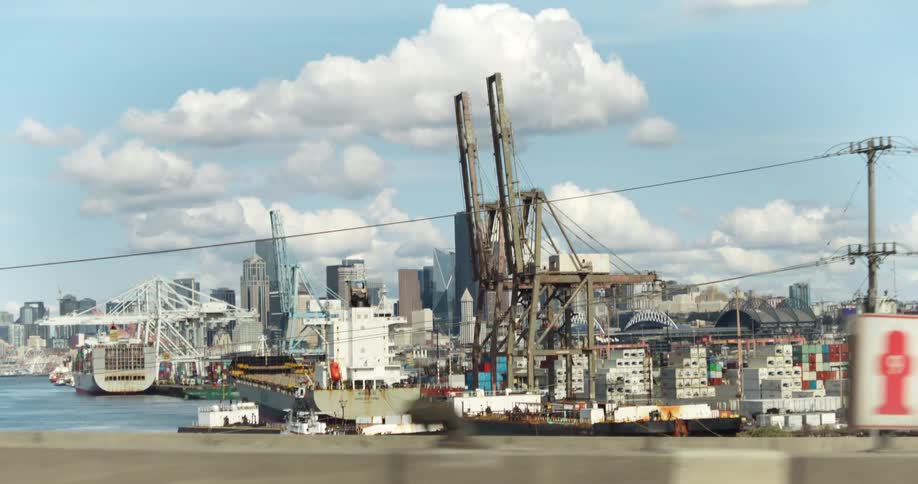 Cargo ships and cranes in a busy port with the city in the background under a blue sky with clouds