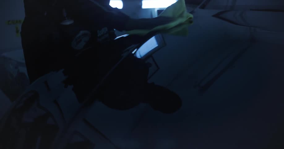 Hands wiping a yellow cloth across the front of a vehicle