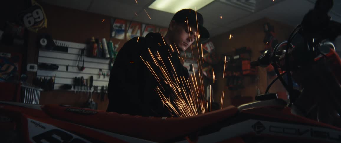 Mechanic using a grinder on a motorcycle inside a workshop generating sparks