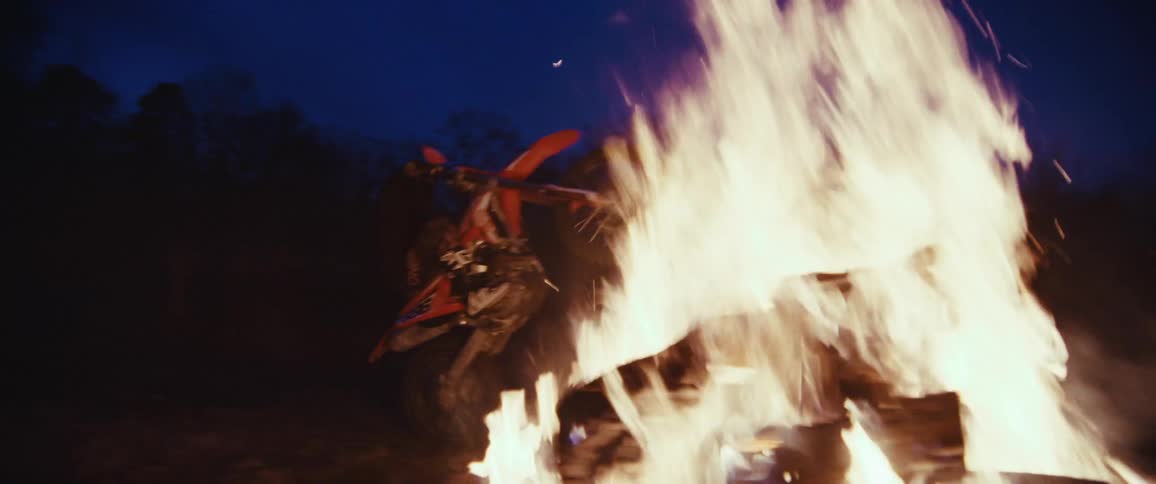 Riding a wheelie on a motorcycle across a bonfire at night