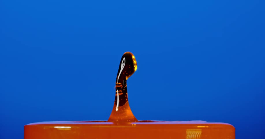 Droplets fall into an orange fluid creating a splash against a blue background