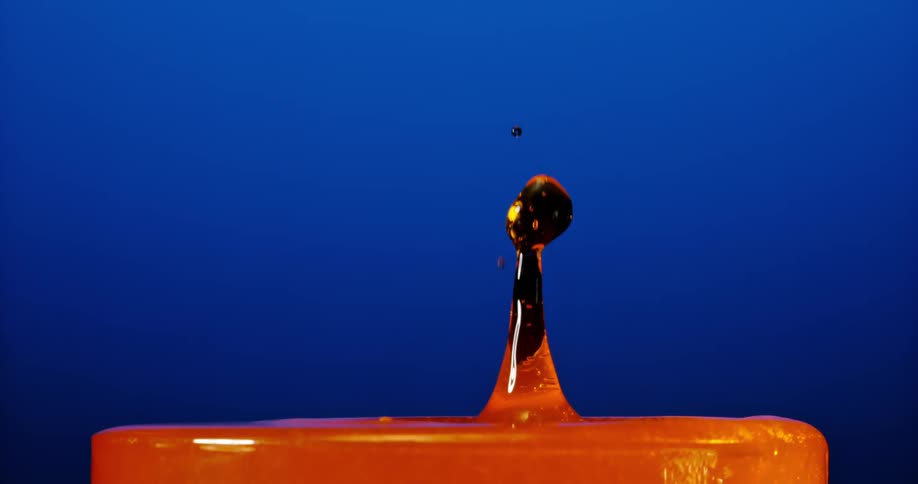 A closeup shot shows a vibrant orange liquid splashing against a deep blue background