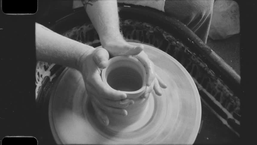 An artist is shaping a clay vase with his hands while using a pottery wheel