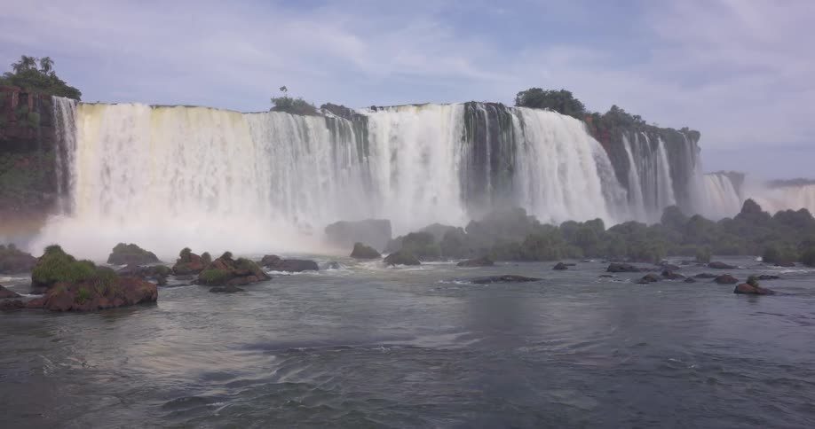 A majestic waterfall plunges over a wide cliff sending mist into the air as the river flows among scattered rocks below