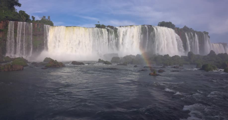 Waterfalls cascade powerfully showcasing a partial rainbow in the mist of the flowing water