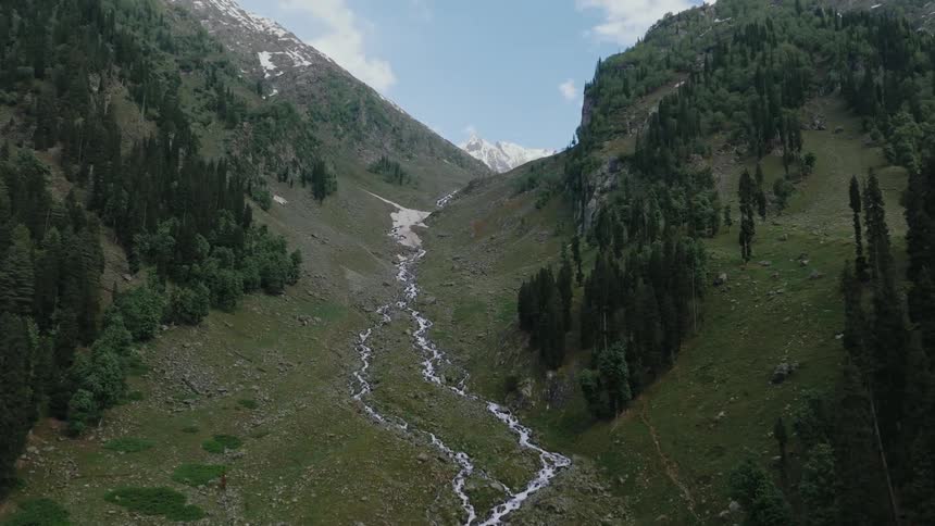 Aerial view flying over a mountain stream flowing through a valley landscape