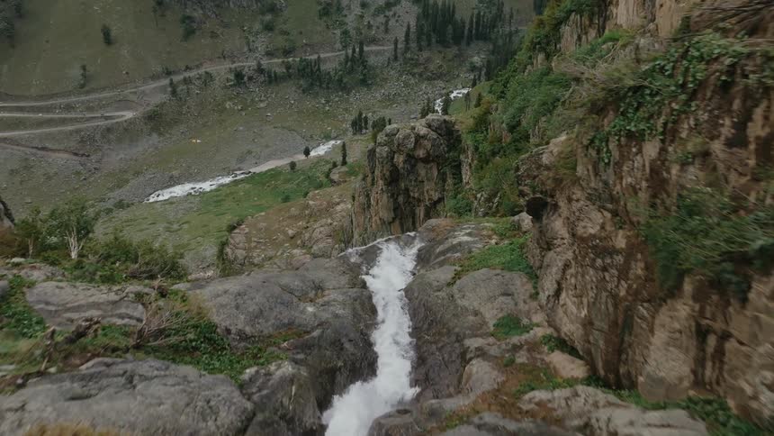 A cascading waterfall flows down a rocky cliffside surrounded by sparse vegetation and rugged terrain