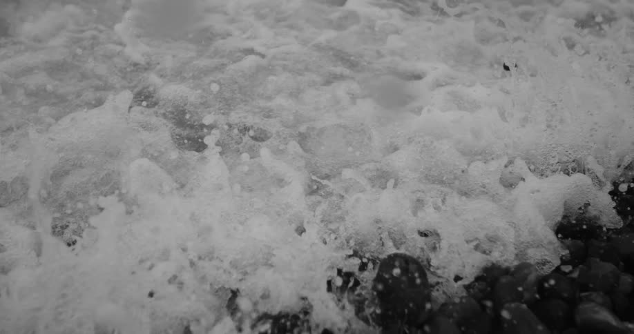 Slowmotion black and white shot of a wave whitewashing as it crashes against a rocky shore