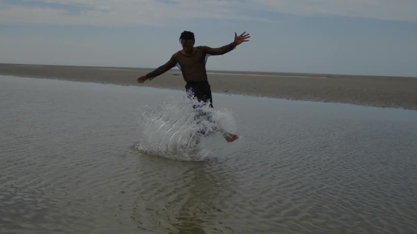 A person splashing through shallow water on a beach kicking water up on a day with muted sunlight