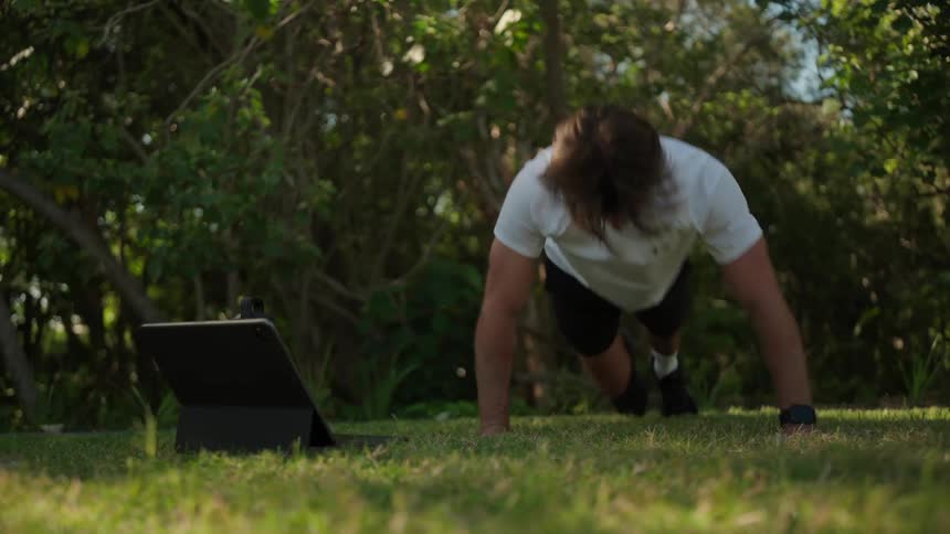 A man is doing pushups outdoors in the grass