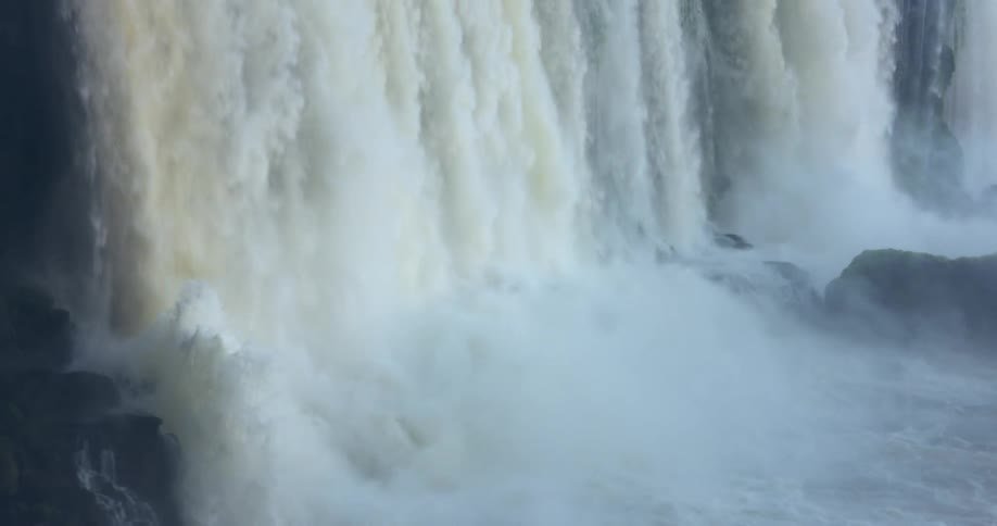 Water powerfully cascades downwards in a large waterfall creating a misty spray and flowing over rocks in a display of natural force
