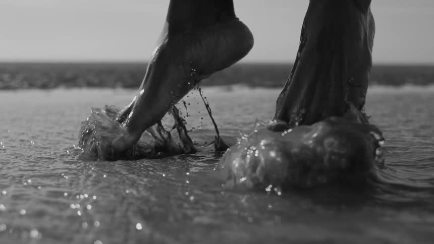 A persons feet in the water jumping up and everything is in black and white tones
