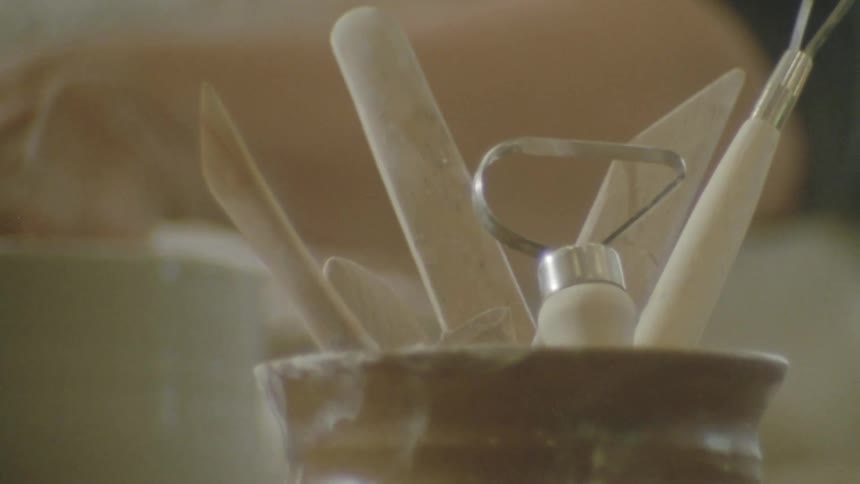 A persons hand picking up a wooden utensil that is among others and has iron tips