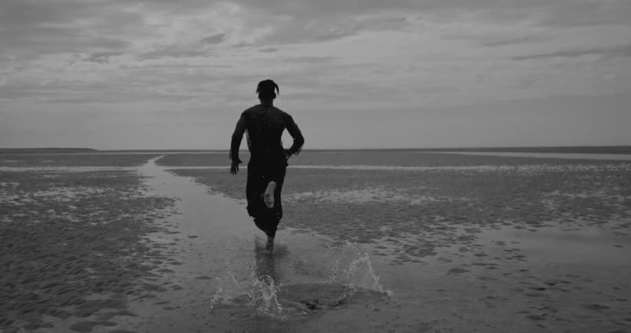 A person wearing a netted longsleeve top runs over puddles of water on a beach