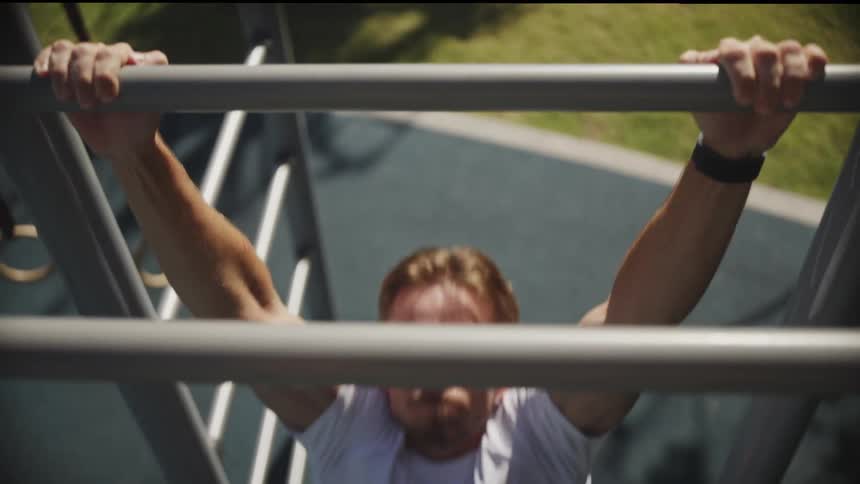 Man in white tshirt does pullup outdoors in sunny park