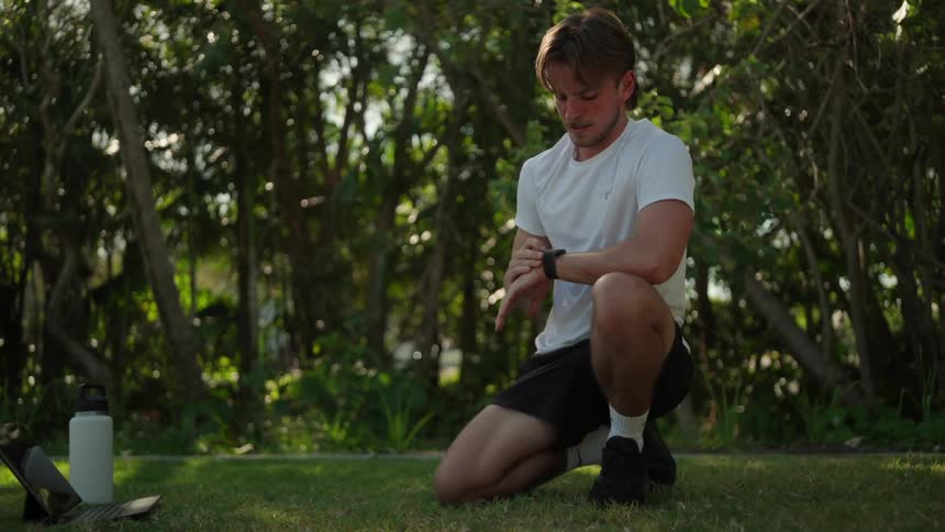 A man kneels in the grass and uses his tablet