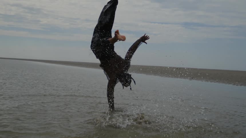 Person doing a somersault with legs suspended in the air in shallow water