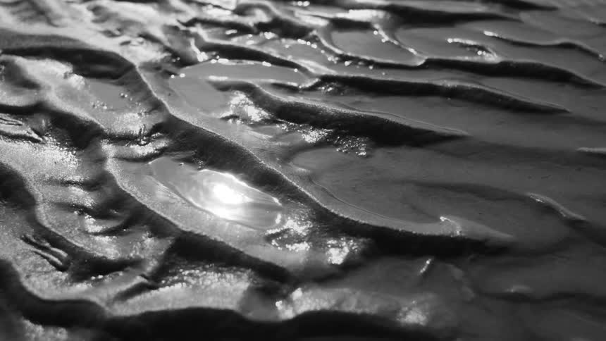 A closeup of wet textured dark sand with intricate patterns and reflections