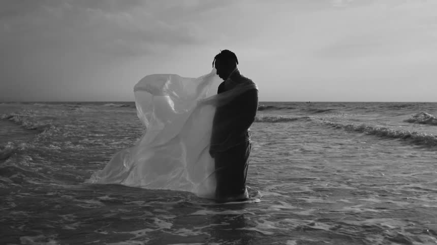 A man is standing in the water covered in a plastic sheet