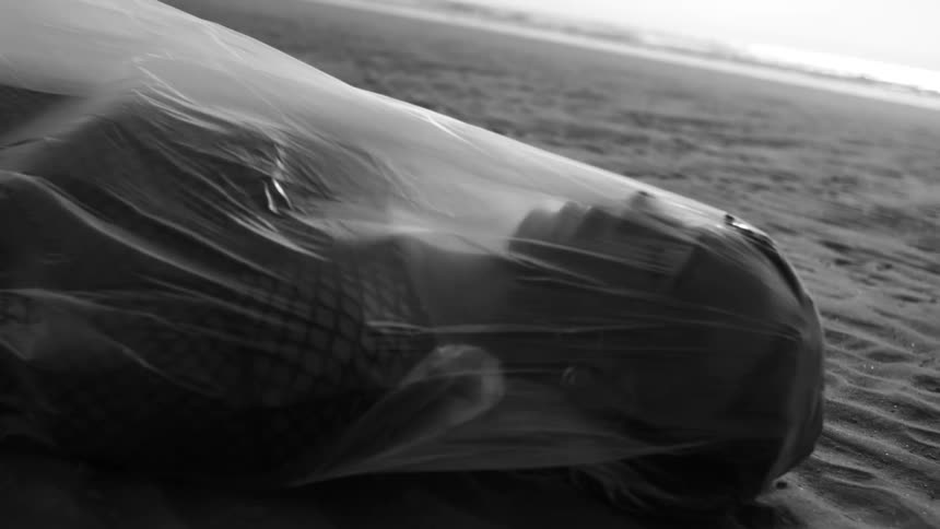 A person lying on a sandy floor wearing a white sheet that is moving in the wind