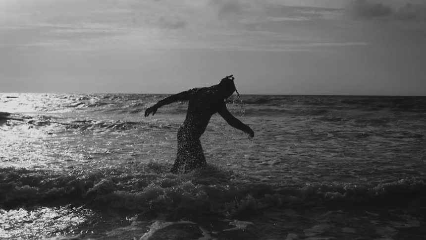 Silhouette of a man walking in kneedeep water along the shallow coast