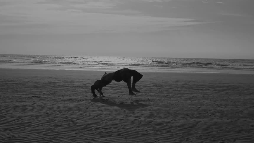 Silhouette of a man doing a backflip on the sand at the beach