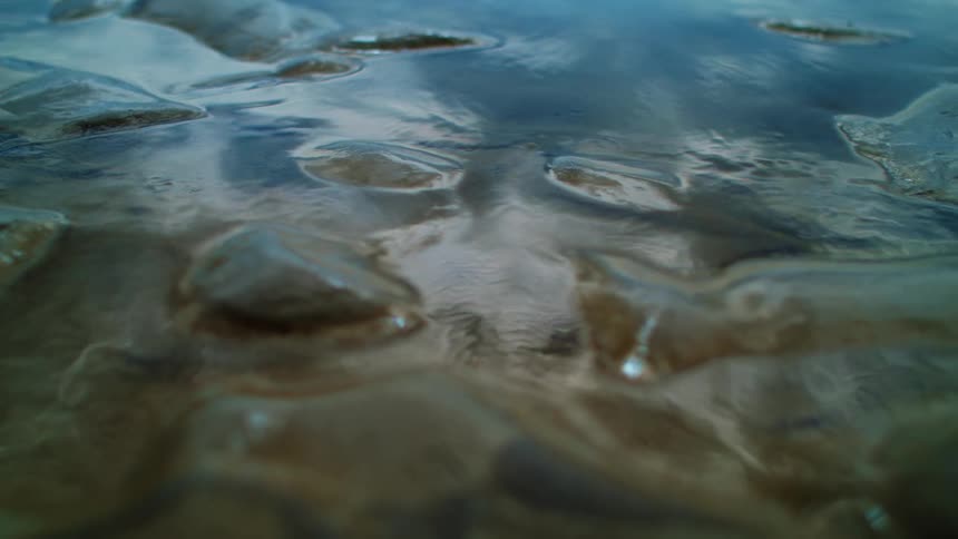 The image shows a closeup view of a wet rocky surface with water pooling in small depressions reflecting the sky above