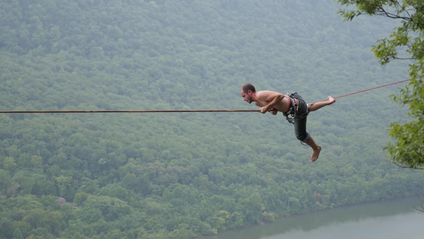 A man hangs from a rope that is suspended over a canyon