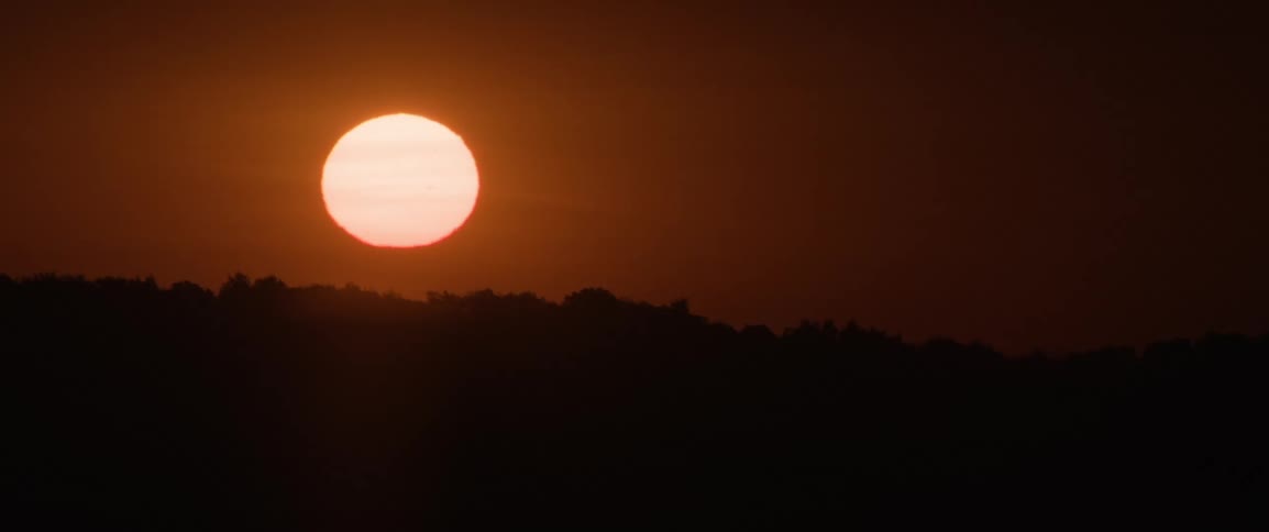 The morning sun glows red as it rises above the horizon