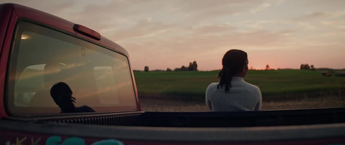 A woman is watching the sunset on the farm while leaning on her truck