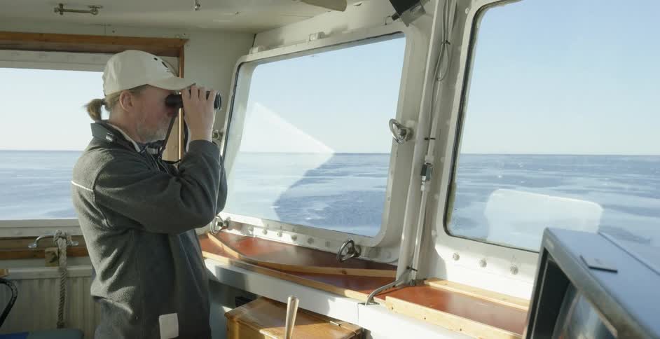 A boat captain uses binoculars to look out of the window