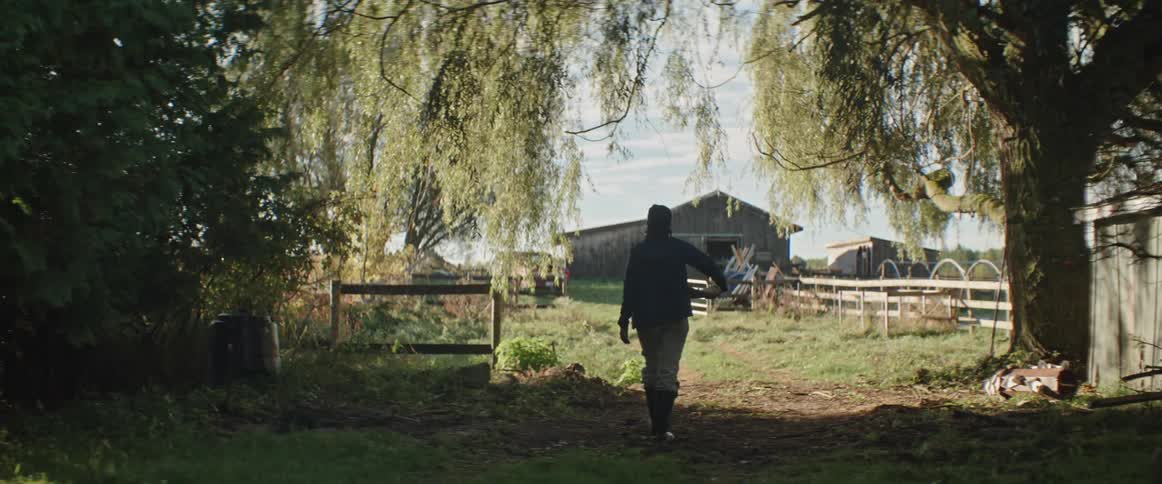 A woman walks in the shade on her farm towards the barn