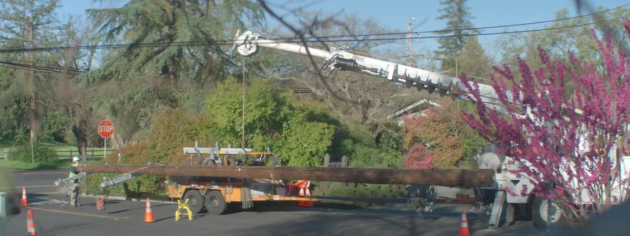 Crane lowering a large utility pole on the street as a truck drives by