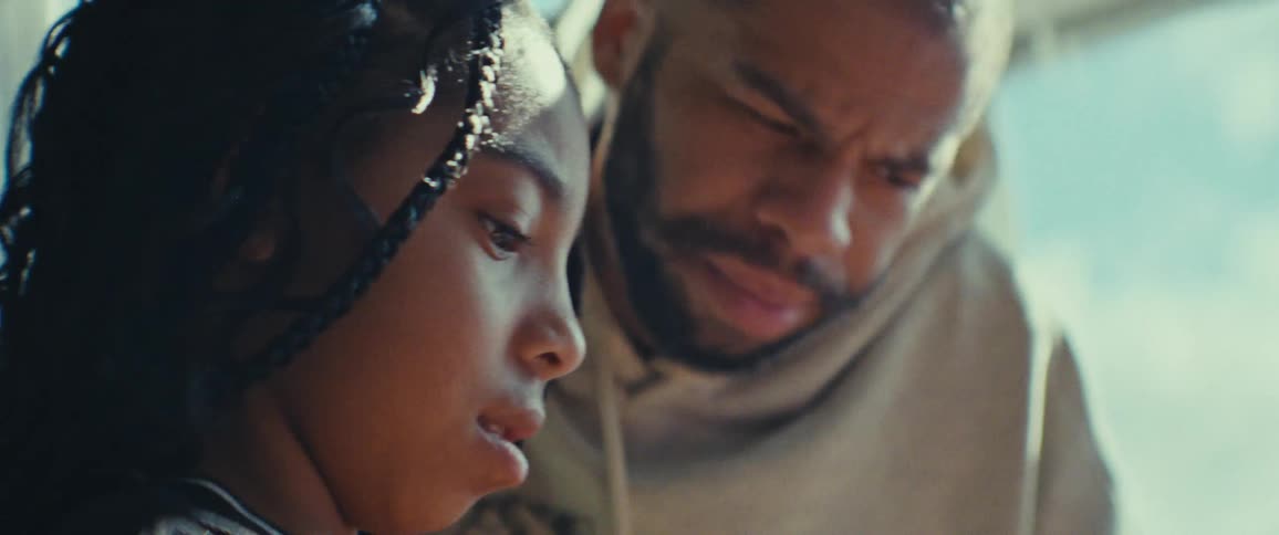 A father helps his daughter with a task in a sunlit room