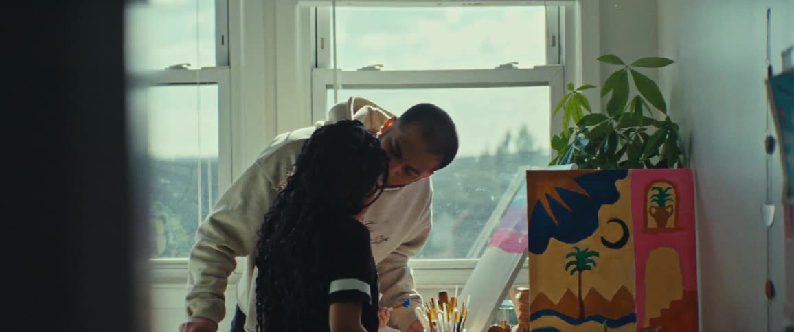 Father kisses his daughter on the forehead in the middle of watching her working on a painting on a sunny day