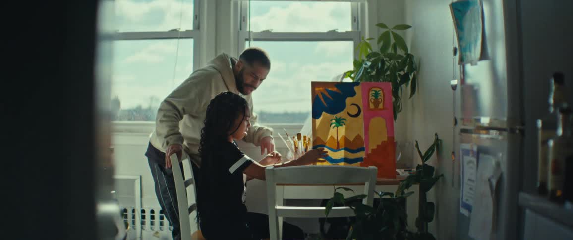 Father standing next to his daughter who is sitting painting